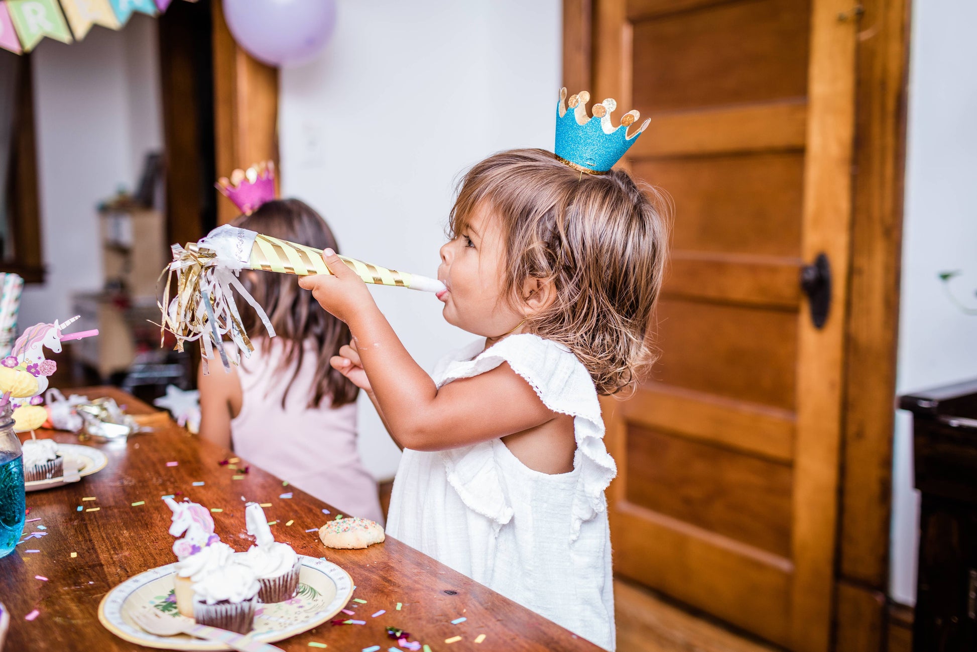 Child with a birthday crown at a party, holding a party horn.